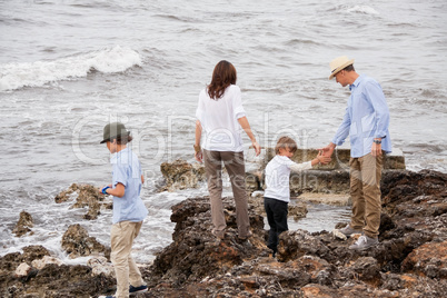 happy family sitting on rock and watching the ocean waves