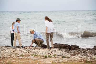 happy family sitting on rock and watching the ocean waves