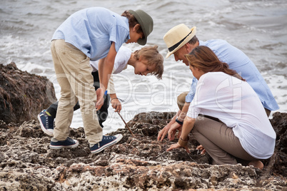 happy family sitting on rock and watching the ocean waves