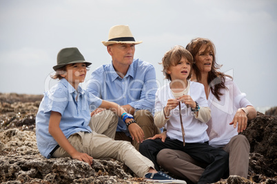happy family sitting on rock and watching the ocean waves