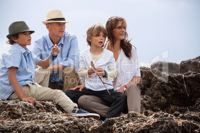 happy family sitting on rock and watching the ocean waves