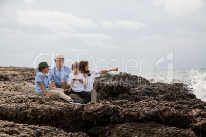 happy family sitting on rock and watching the ocean waves