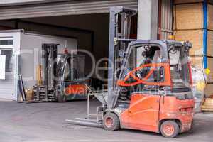 Small orange forklift parked at a warehouse