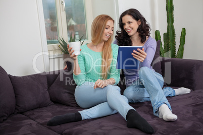 two young attractive girl with tablett pc on couch