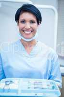 Female dentist in blue scrubs holding tray of tools