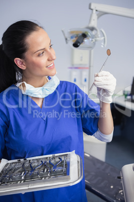 Smiling dentist holding tray and looking angle mirror