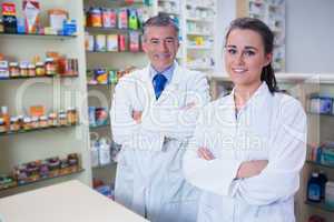 Smiling pharmacist and his trainee with arms crossed