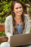 Smiling student sitting on bench listening music and holding lap