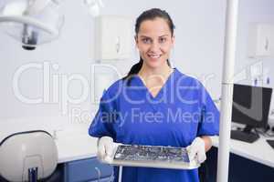 Portrait of a smiling dentist holding tray with equipment