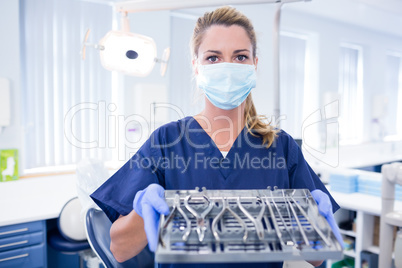 Dentist in blue scrubs holding tray of tools