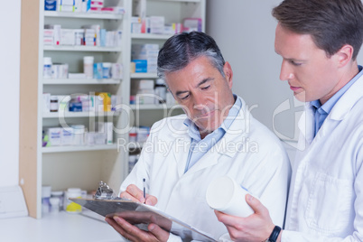 Man holding medication and his colleague writing a prescription