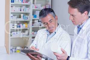 Man holding medication and his colleague writing a prescription