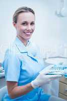 Female dentist in blue scrubs holding tray of tools
