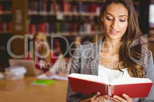 Pretty brunette student standing and reading book