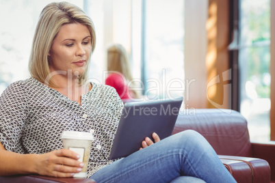 Woman using digital tablet and holding disposable cup
