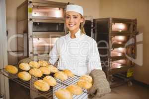 Baker smiling at camera holding rack of rolls