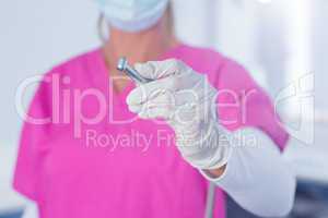 Dentist in surgical mask and scrubs holding tool