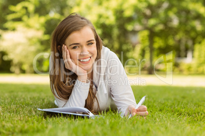 Smiling university student lying and writing on notepad