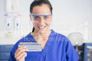 Smiling dentist with safety glasses holding teeth whitening