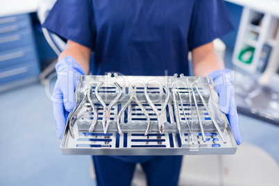 Dentist in blue scrubs holding tray of tools