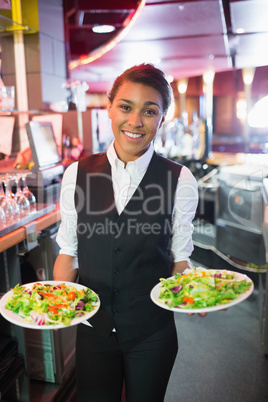 Pretty barmaid holding plates of salads