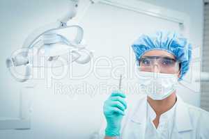 Dentist in surgical mask and safety glasses holding hook
