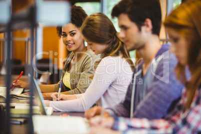 Student looking at camera while studying with classmates Student looking at camera while studying with classmates