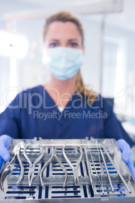 Dentist in blue scrubs holding tray of tools