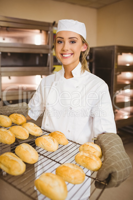 Baker smiling at camera holding rack of rolls