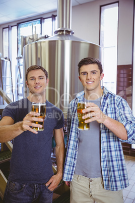 Young men holding a pint of beer smiling at camera