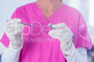 Dentist in pink scrubs holding tool