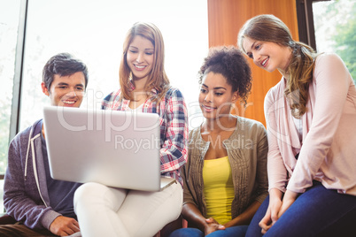 Smiling students sitting on couch using laptop