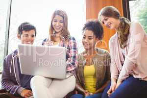 Smiling students sitting on couch using laptop