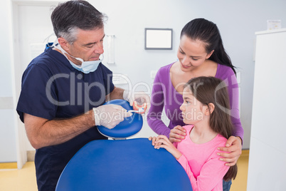 Dentist explaining to young patient and her mother how use tooth