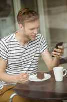 Smiling student with chocolate cake using smartphone