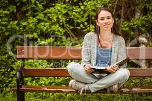 Smiling student sitting on bench listening music with mobile pho