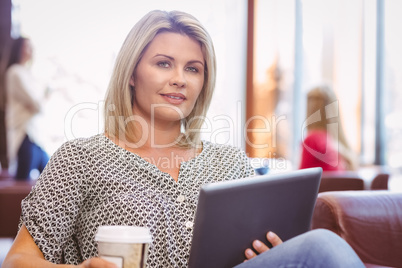 Smiling woman using digital tablet and holding disposable cup