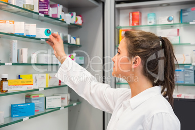 Junior pharmacist taking medicine from shelf