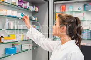Junior pharmacist taking medicine from shelf