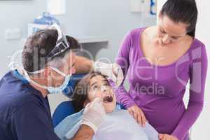 Pediatric dentist examining young patient with her mother