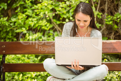 Smiling student sitting on bench listening music and using lapto