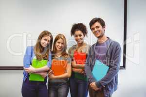 Students standing and smiling at camera holding notepads