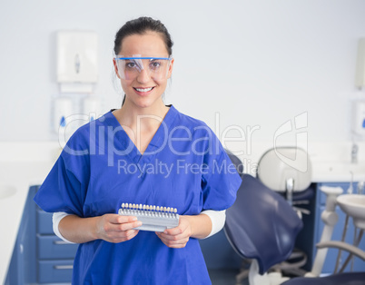 Smiling dentist with safety glasses holding teeth whitening
