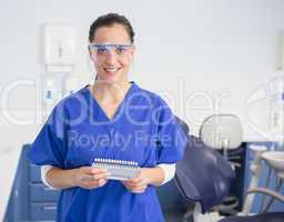 Smiling dentist with safety glasses holding teeth whitening