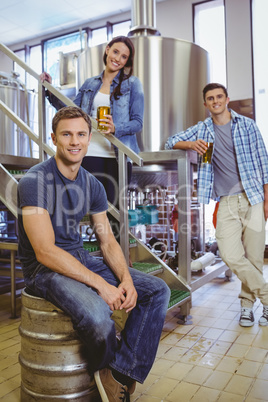 Man siting on keg and his colleague holding a glass of beer