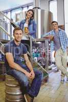 Man siting on keg and his colleague holding a glass of beer