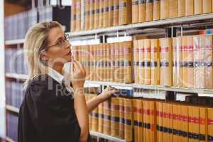 Lawyer wearing glasses and looking for a book in the shelf