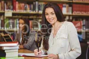 Smiling pretty brunette student writing in notepad