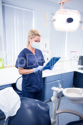 Dentist in mask and blue scrubs using her tablet