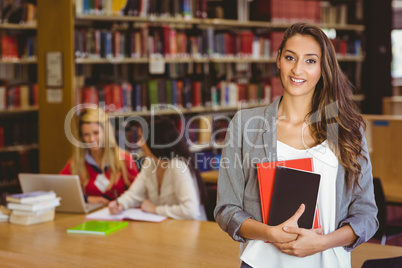 Pretty student holding books with classmates behind her